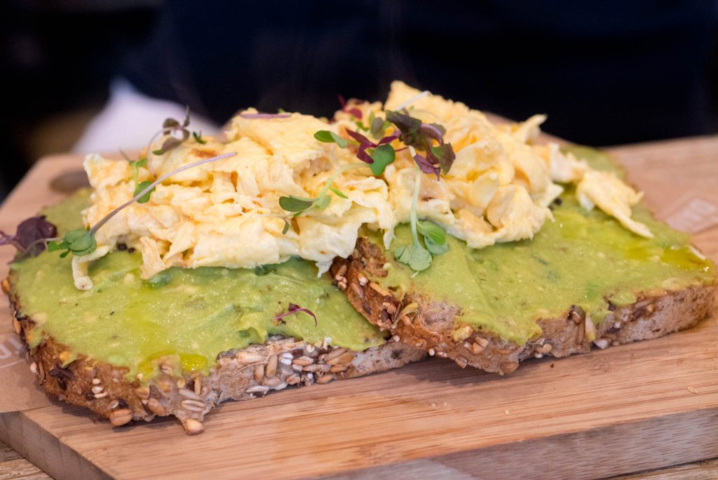 a wooden cutting board topped with a piece of bread covered in guacamole.