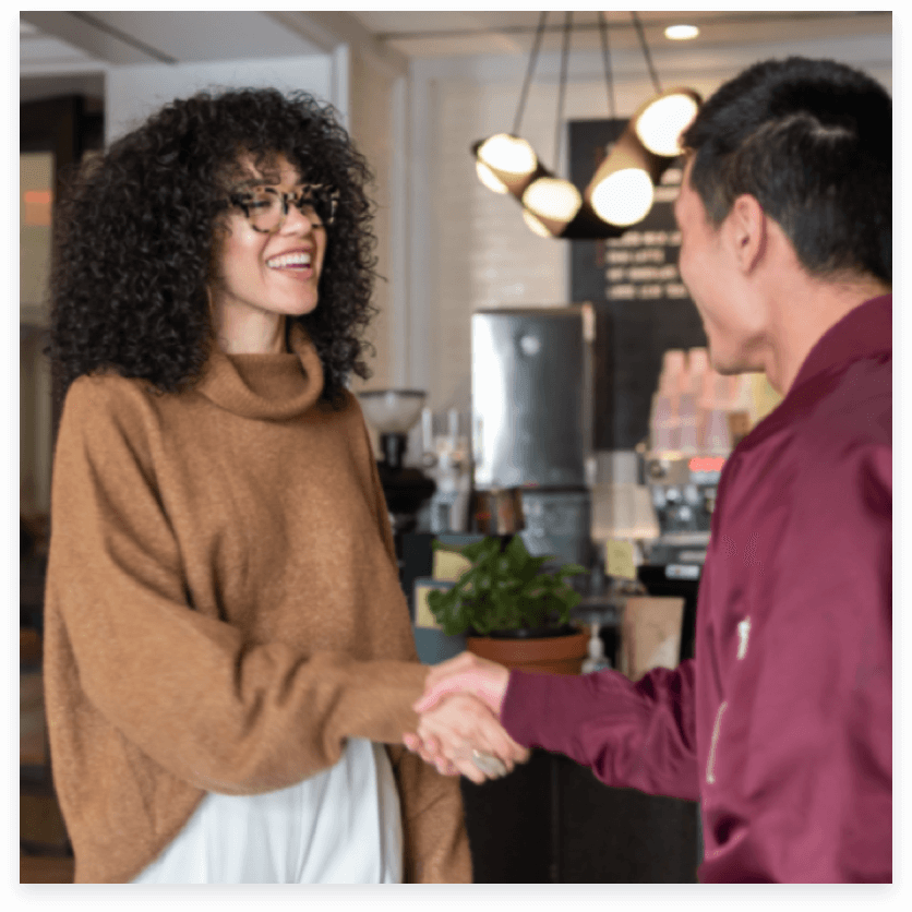 a man and a woman shaking hands in a kitchen.