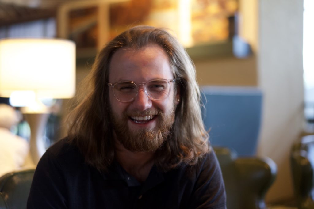 a man with long hair and glasses smiling.