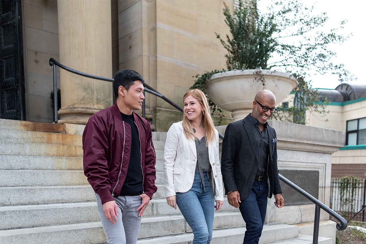 Three people standing on steps in front of a building.