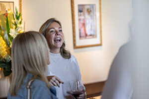 Two women laughing while holding wine glasses in a room.
