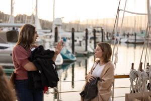 Two women standing on a boat talking to each other.