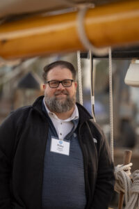 A man wearing glasses and a jacket standing on a boat.