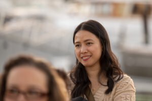 A woman smiles while sitting at a table next to a boat.