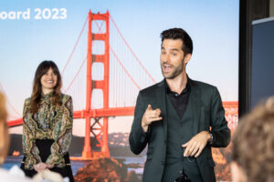 A man is giving a presentation in front of a golden gate bridge.