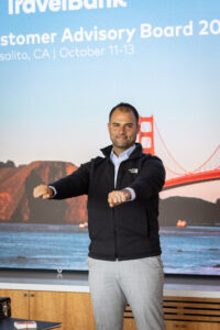 A man standing in front of a screen with the words travelbank customer advisory board.