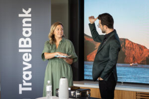 A man and woman standing in front of a travel bank screen.