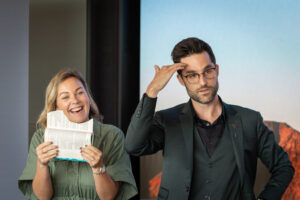 A man and woman holding up a piece of paper in front of a screen.