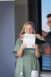 A man and woman holding up a piece of paper in front of a screen.