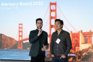 Two men standing in front of a screen showing the golden gate bridge.