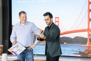 Two men standing in front of a screen with a golden gate bridge in the background.