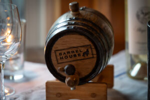A wooden barrel on a table next to a glass of wine.