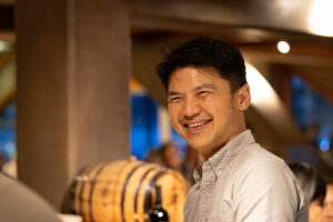 A man smiling in front of a wine barrel.