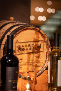 Two bottles of wine sit next to a wooden barrel.